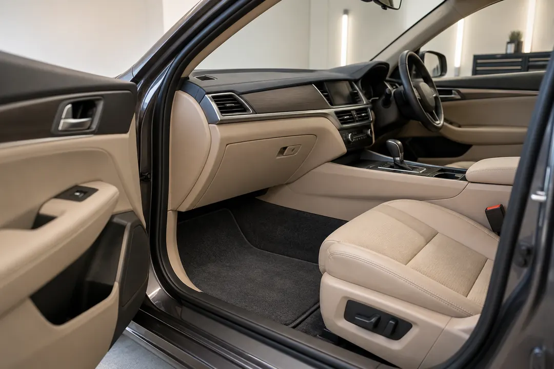 An open passenger door reveals a freshly detailed tan car seat and charcoal floor mat in a softly lit detailing bay.